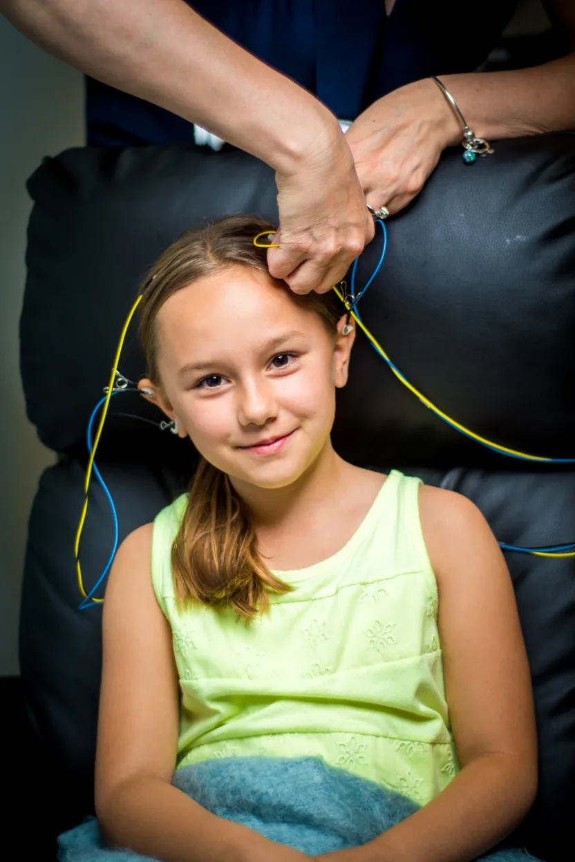 A smiling girl with NeurOptimal sensors on, while an adult attaches a sensor