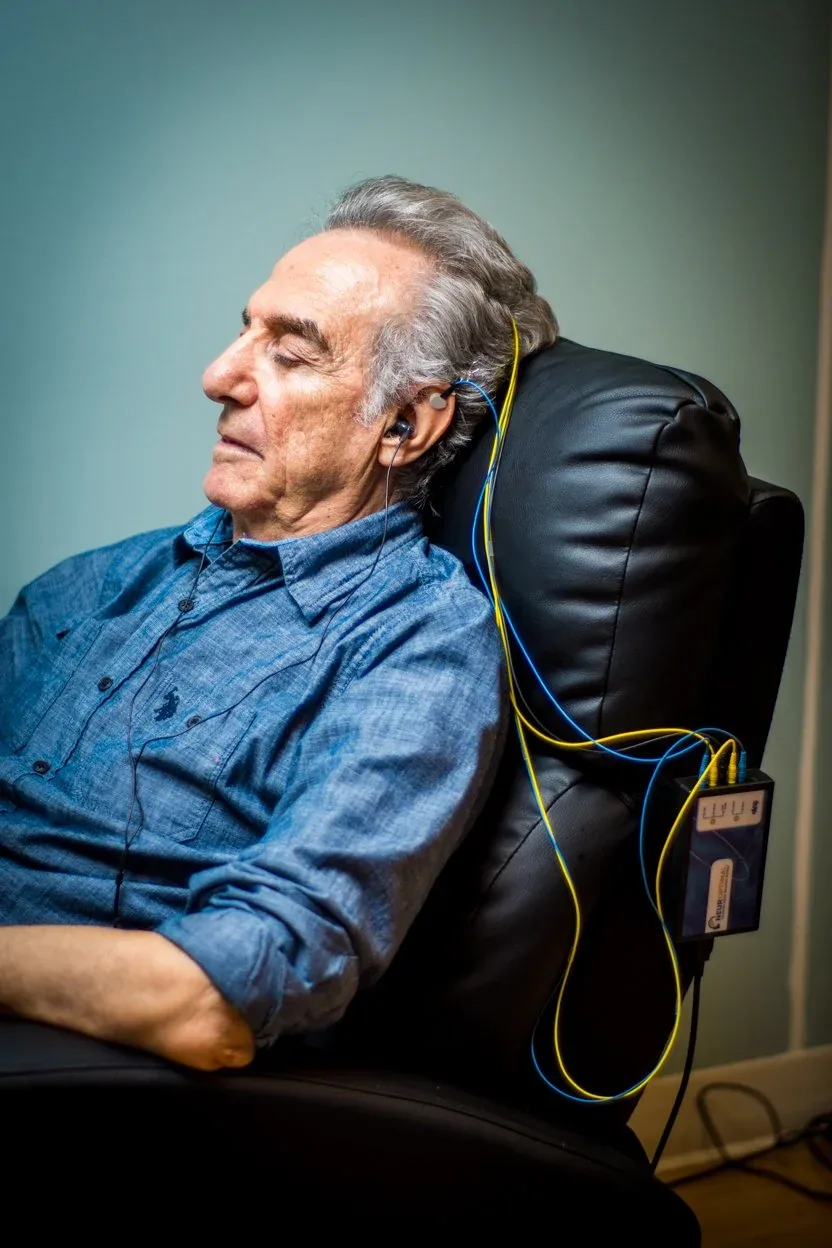 An older man resting in a recliner with NeurOptimal sensors and earbuds on